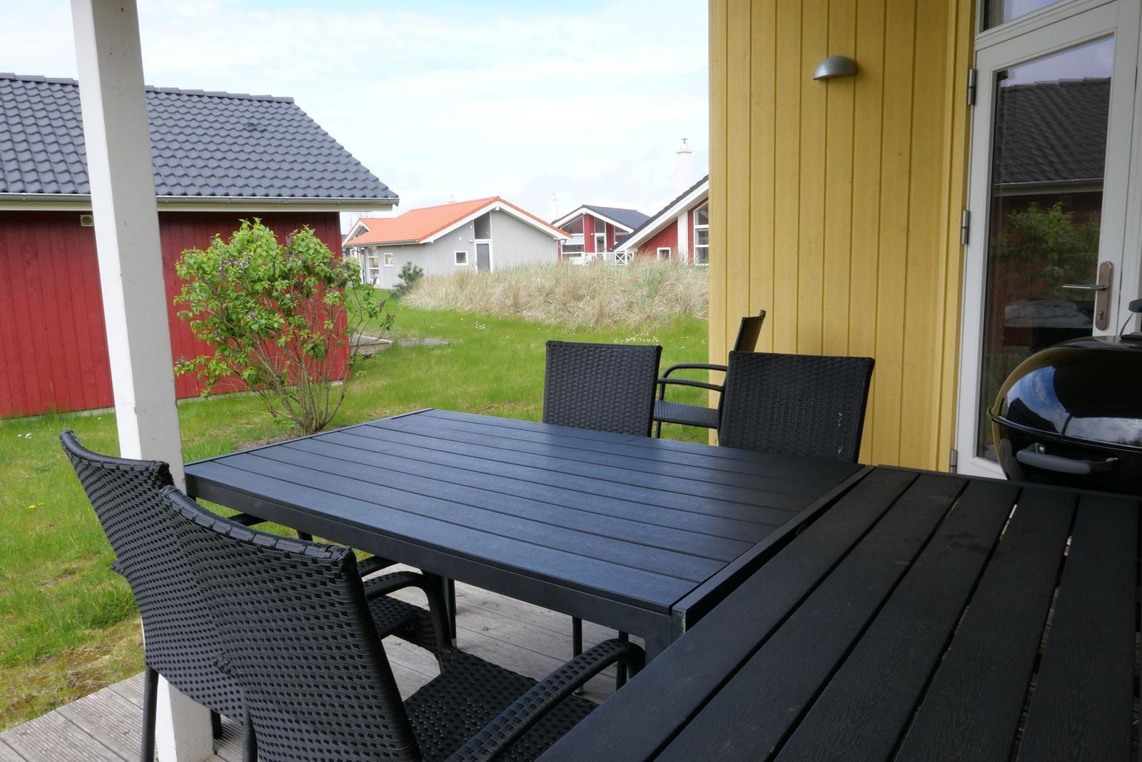 Terrasse mit Tisch und Stühlen, Grill und Blick auf Grünfläche und Häuser.