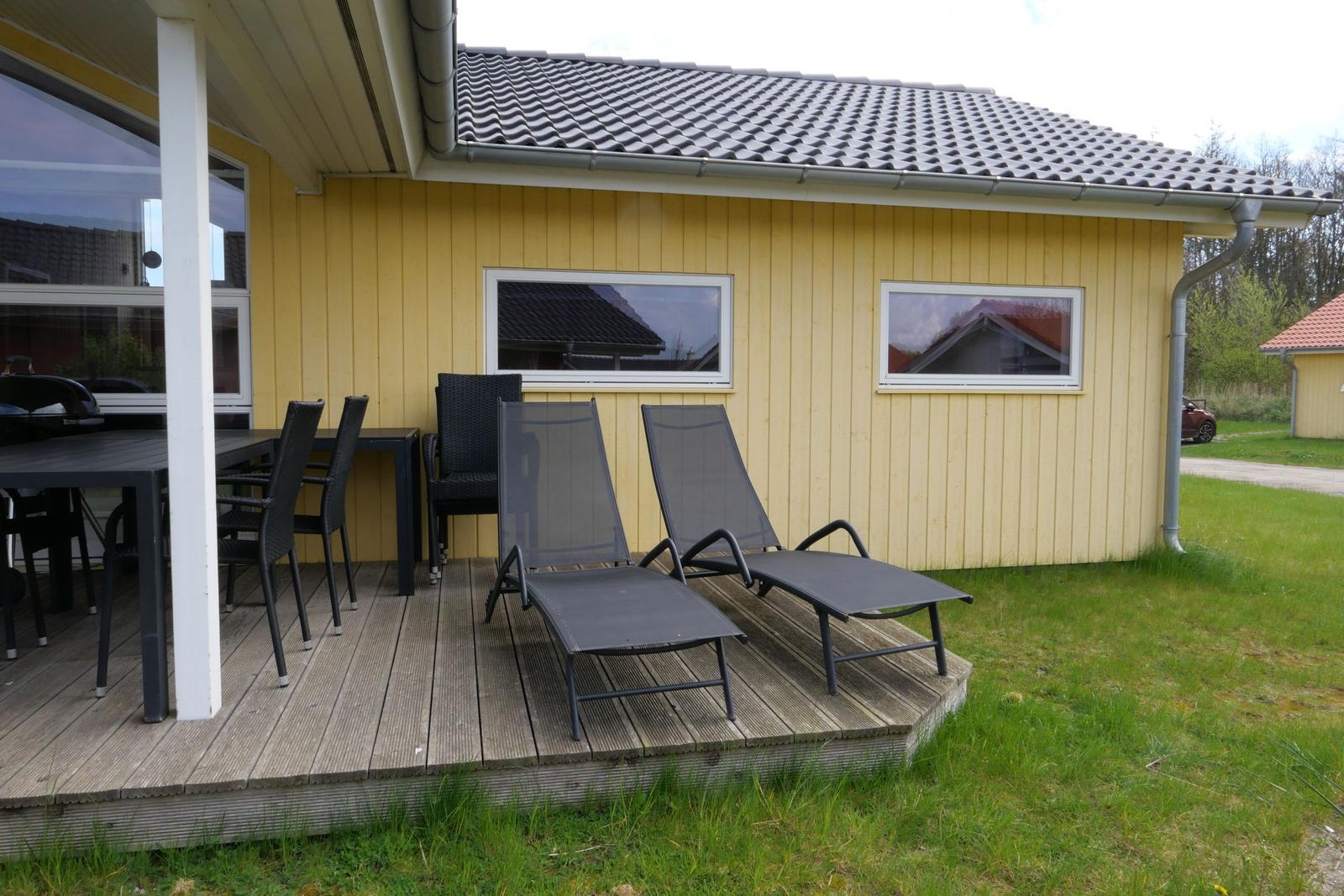 Terrasse mit Tisch, Stühlen und Liegen vor gelbem Haus mit Dach