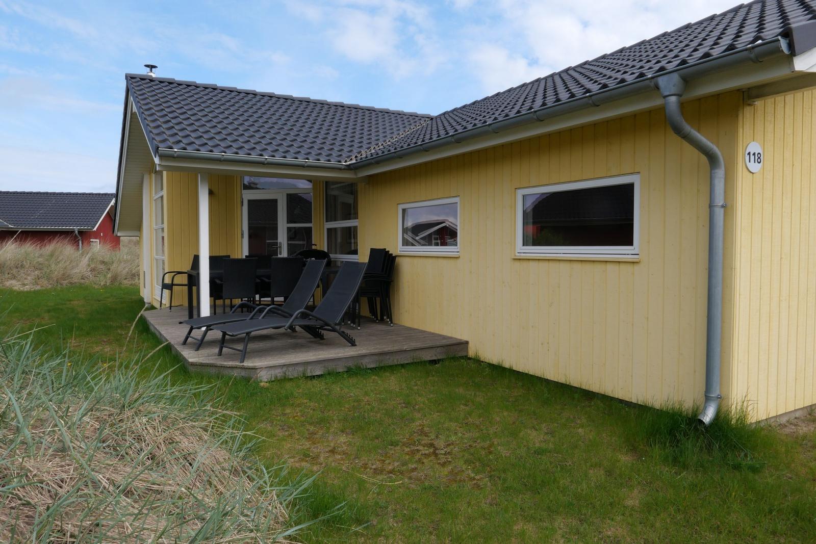 Gelbes Ferienhaus mit Terrasse, Liegen und Garten. Hausnummer 118.