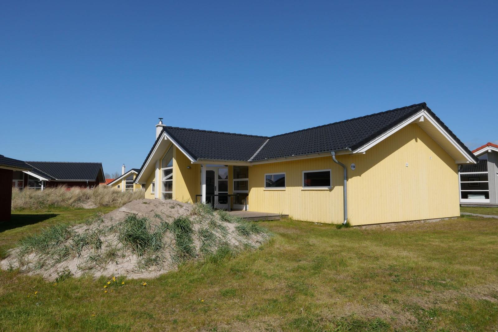 Ein gelbes Ferienhaus mit schwarzem Dach und Garten. Nummer 118.