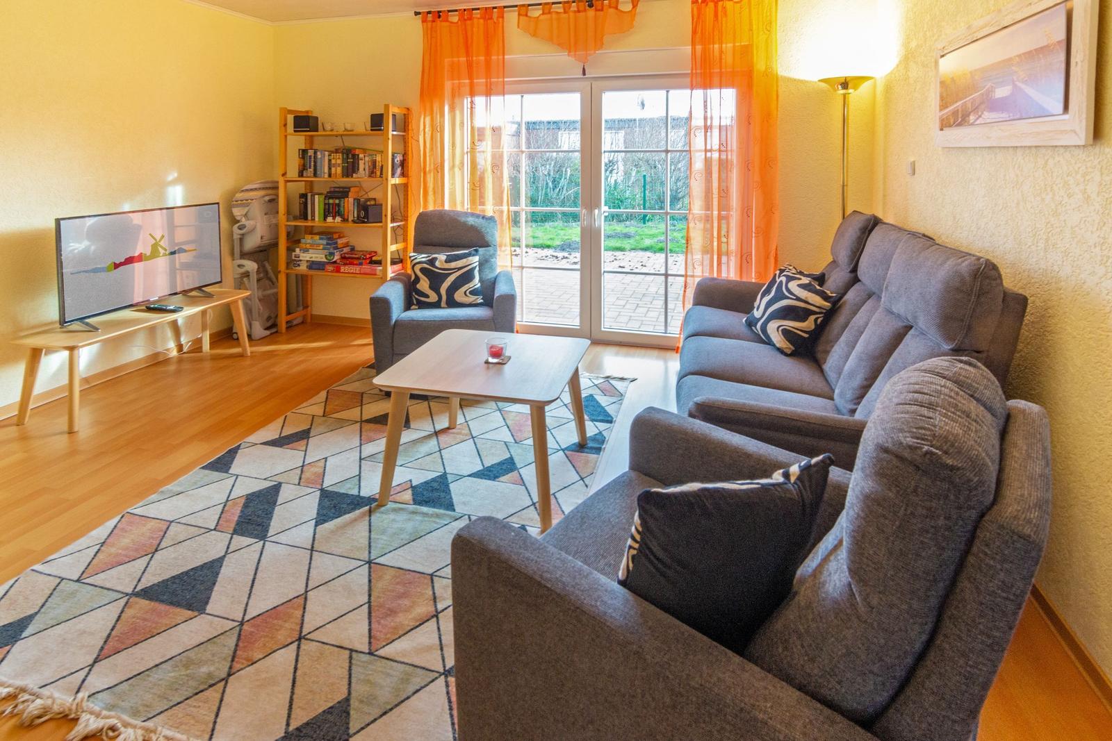 Wohnzimmer mit Sofa, Sessel, Fernseher und Terrassentür.
