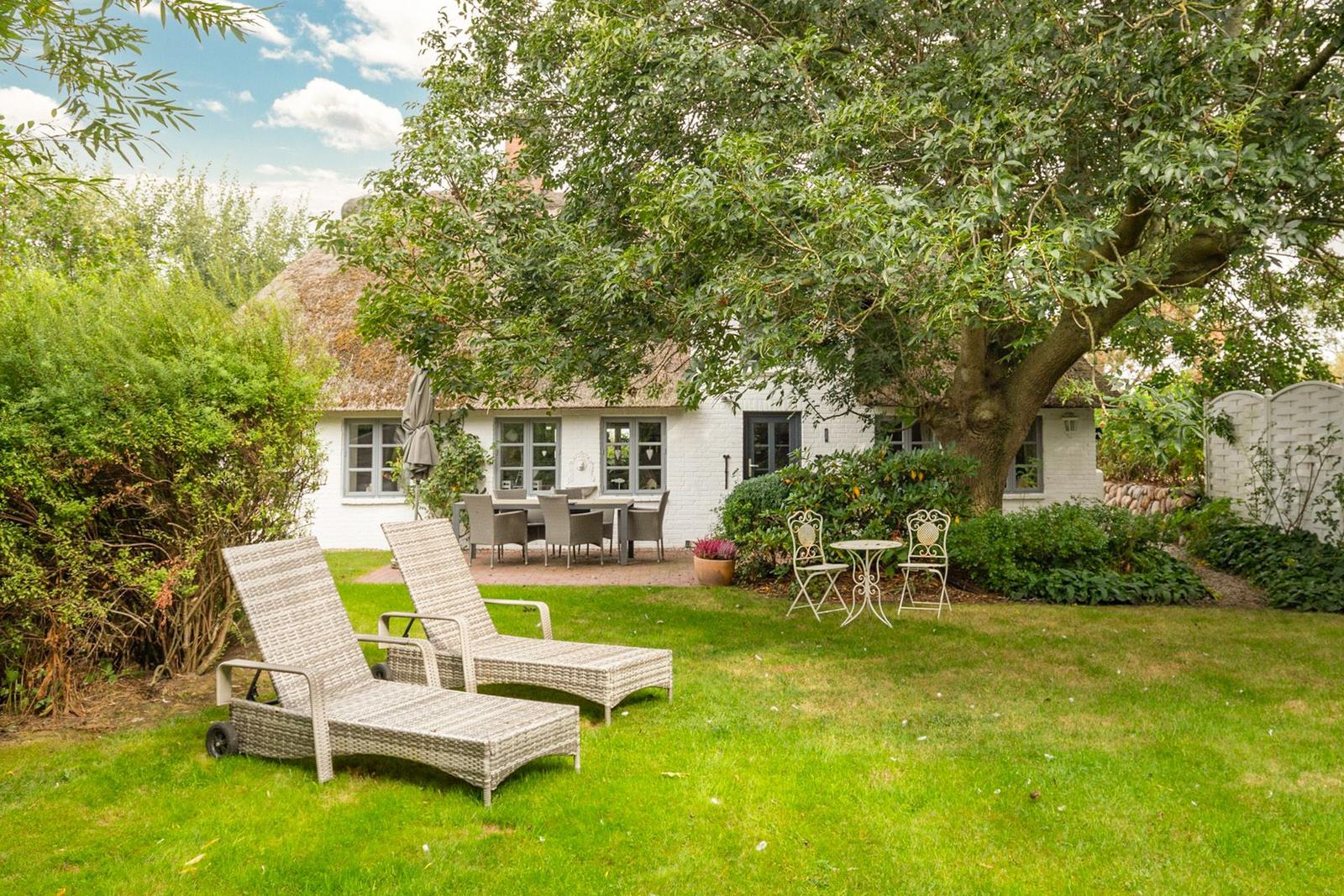 Haus mit Garten, Sonnenliegen und Tisch unter Bäumen.