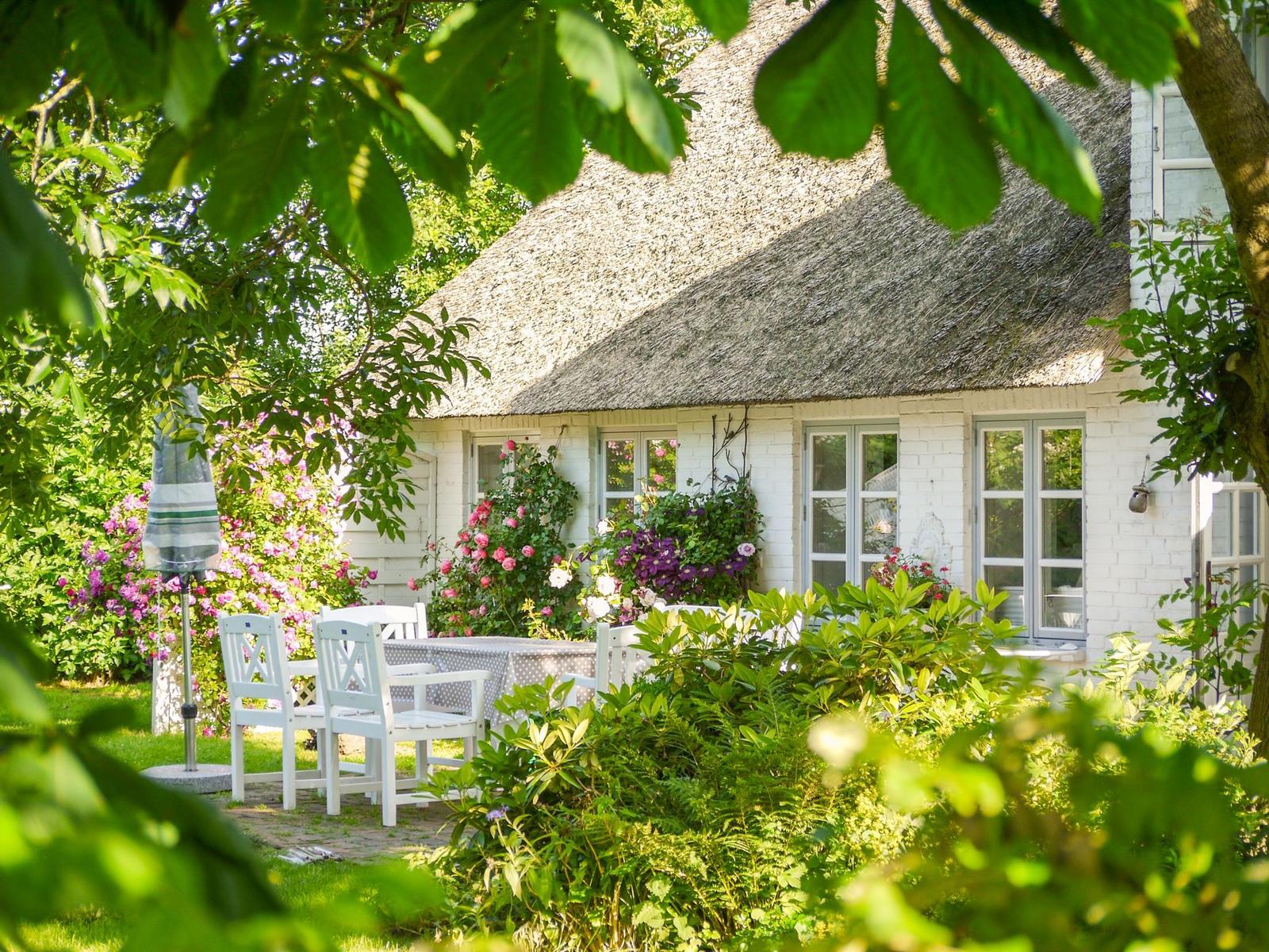 Weiße Villa mit Strohdach, Garten mit Tisch und Stühlen, Blumen und Bäume.