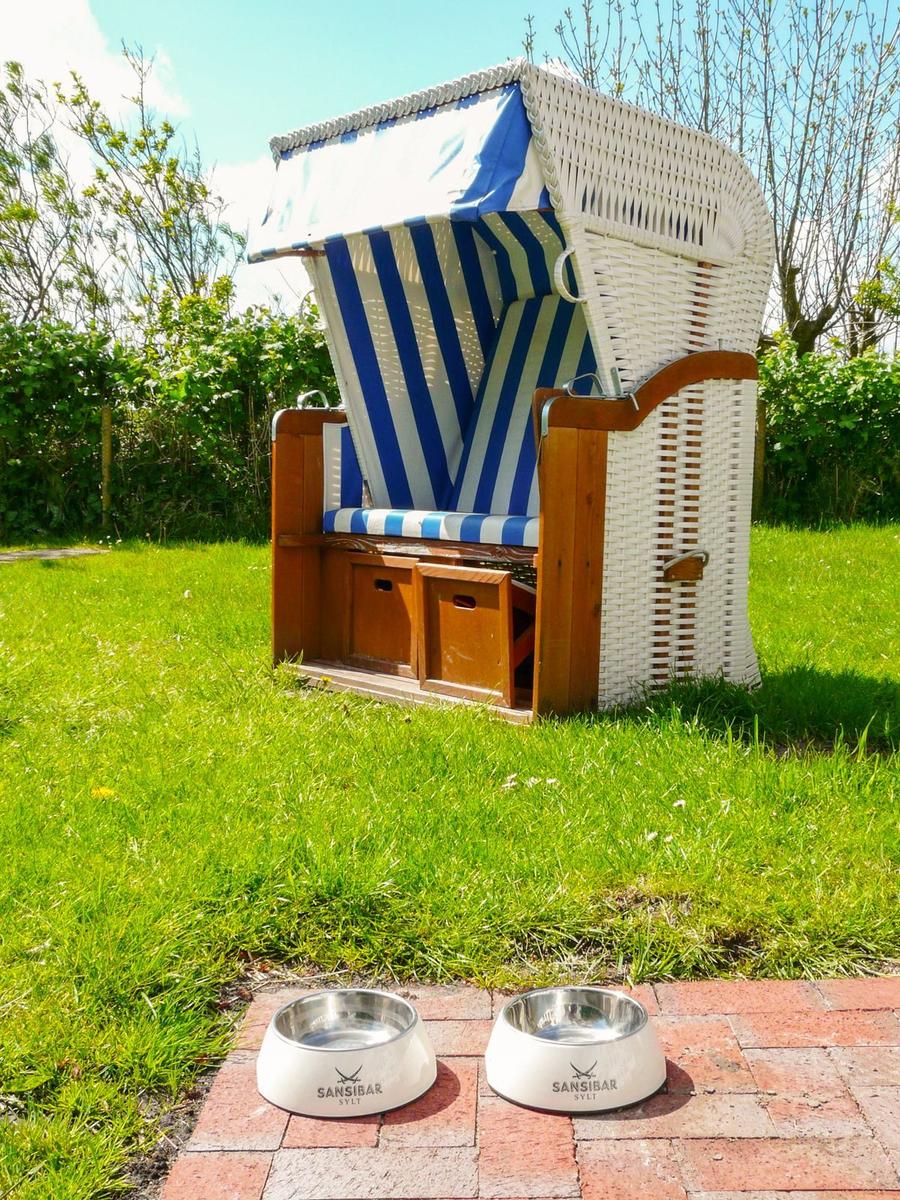 Strandkorb mit blau-weißem Stoff und zwei Metallfuttertassen auf Steinplatten.
