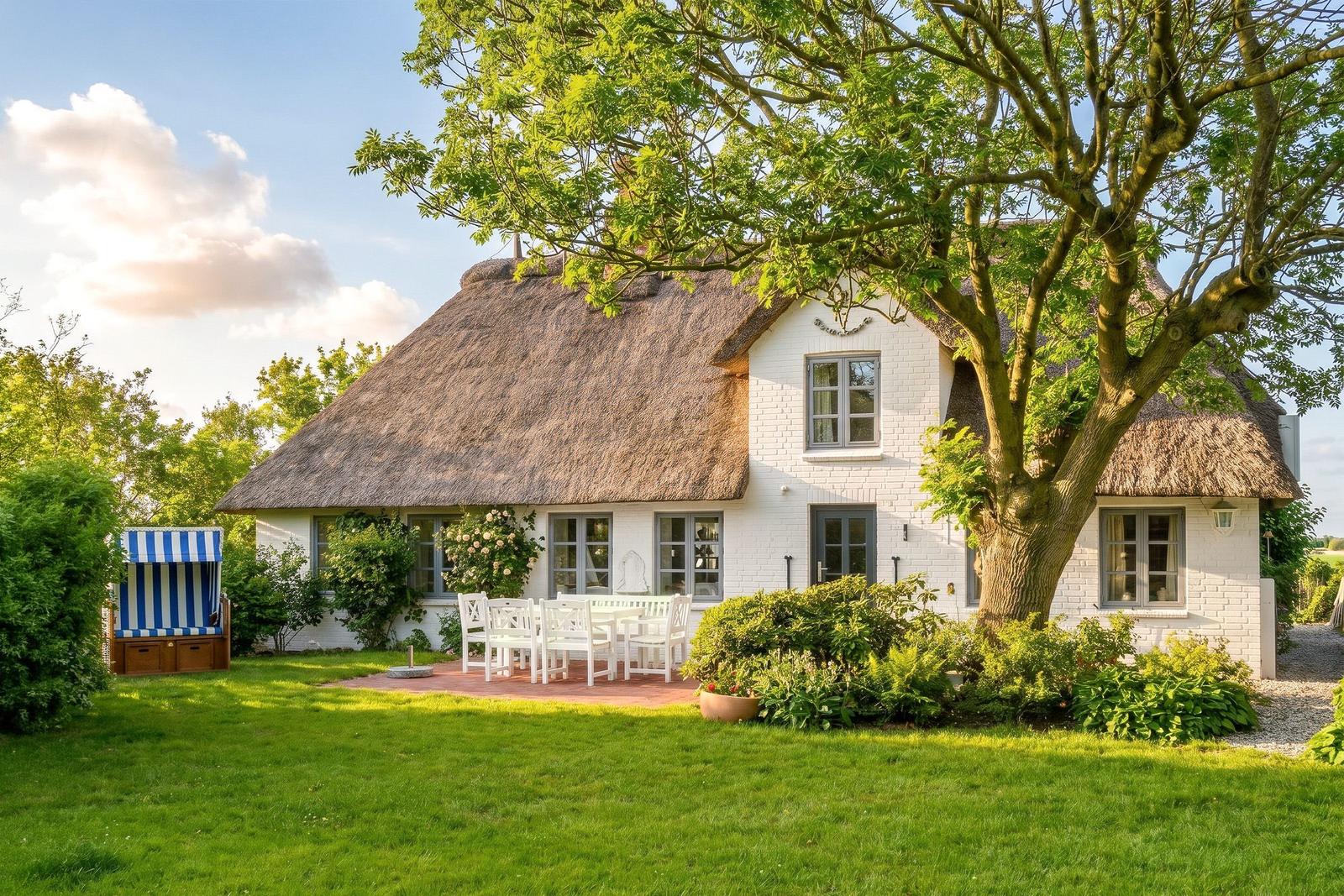 Wohnhaus mit Strohdach, weißer Fassade und Garten mit Tisch und Stühlen.