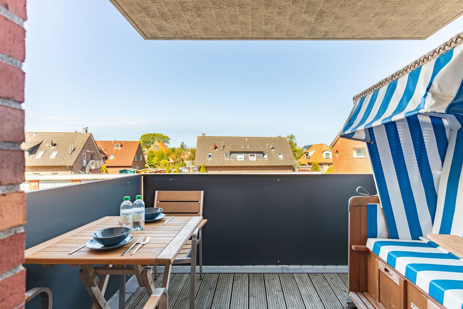 Terrace with table, chairs, and blue-white sunshade. View of houses and sky.