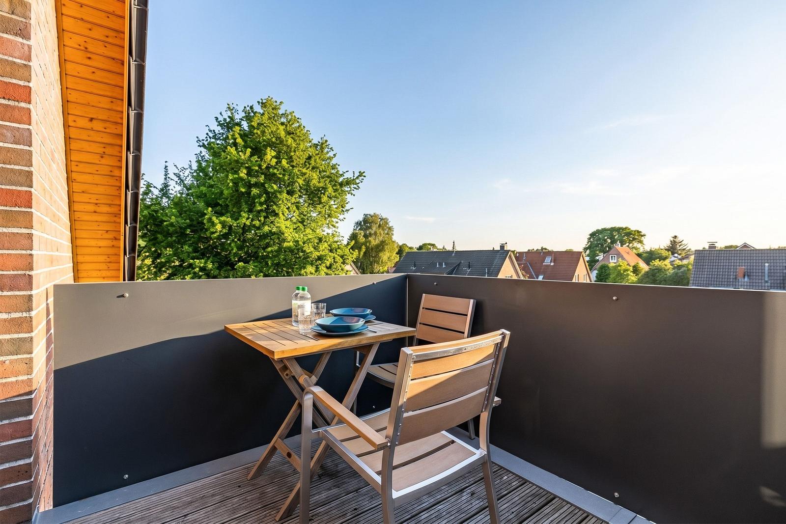 Terrace with table and two chairs, view of trees and rooftops.