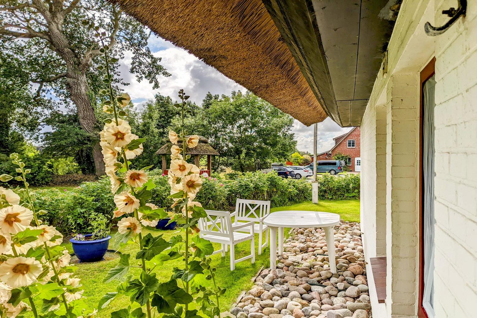 Terrasse mit weißem Tisch und Stühlen, umgeben von Blumen und Steinweg.