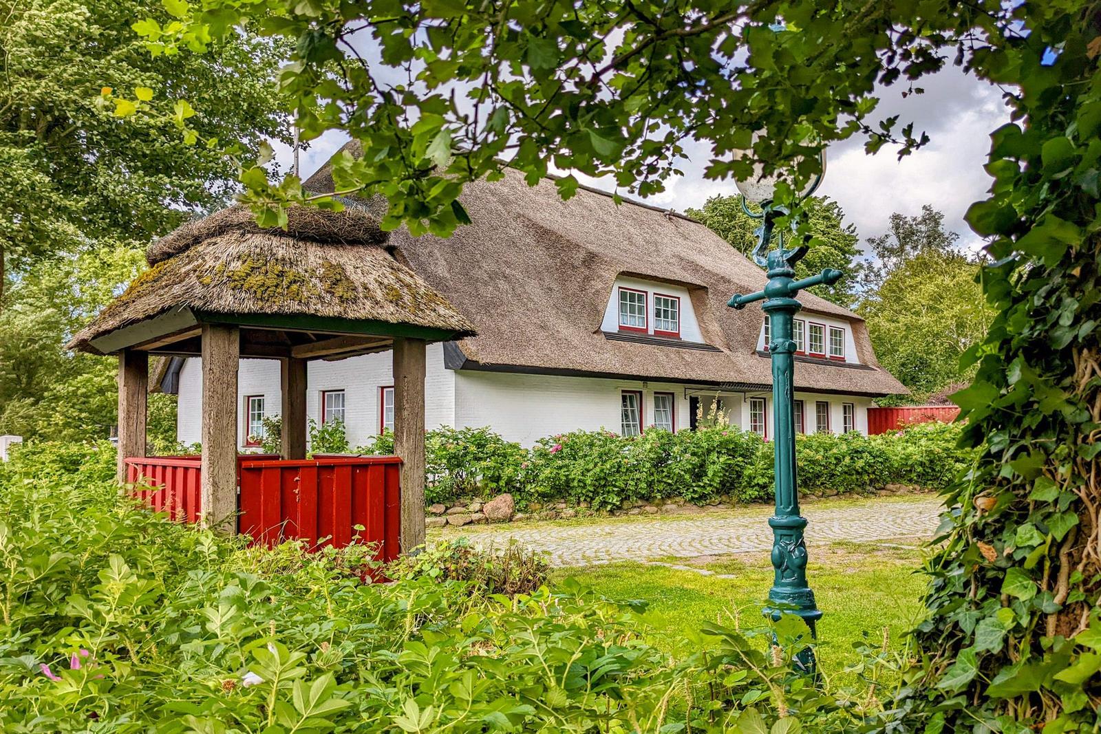 Ein weißes Haus mit Strohdach, umgeben von Grün und einem roten Pavillon.