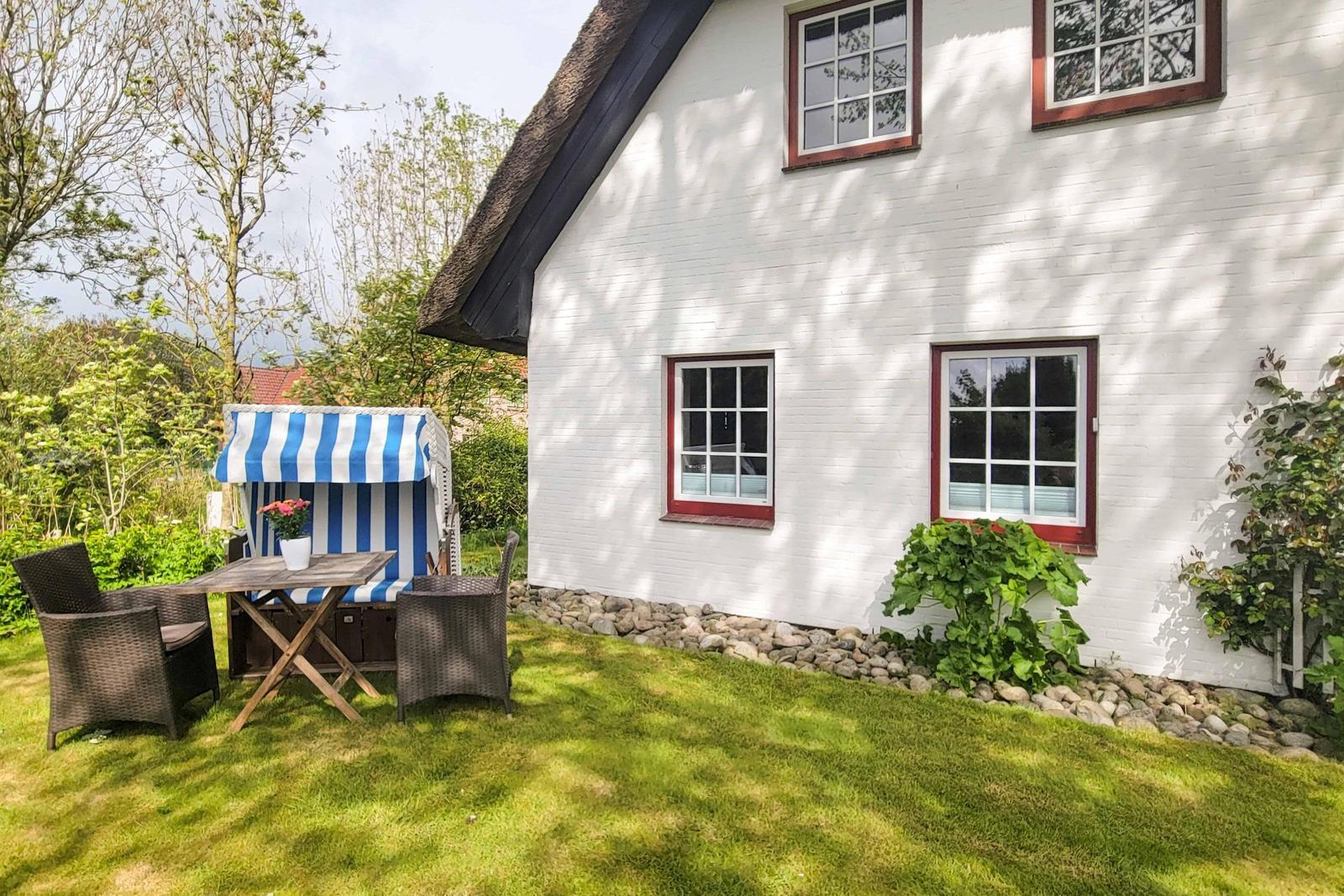Weiße Hauswand mit roten Fensterrahmen und Gartenbereich mit Strandkorb.