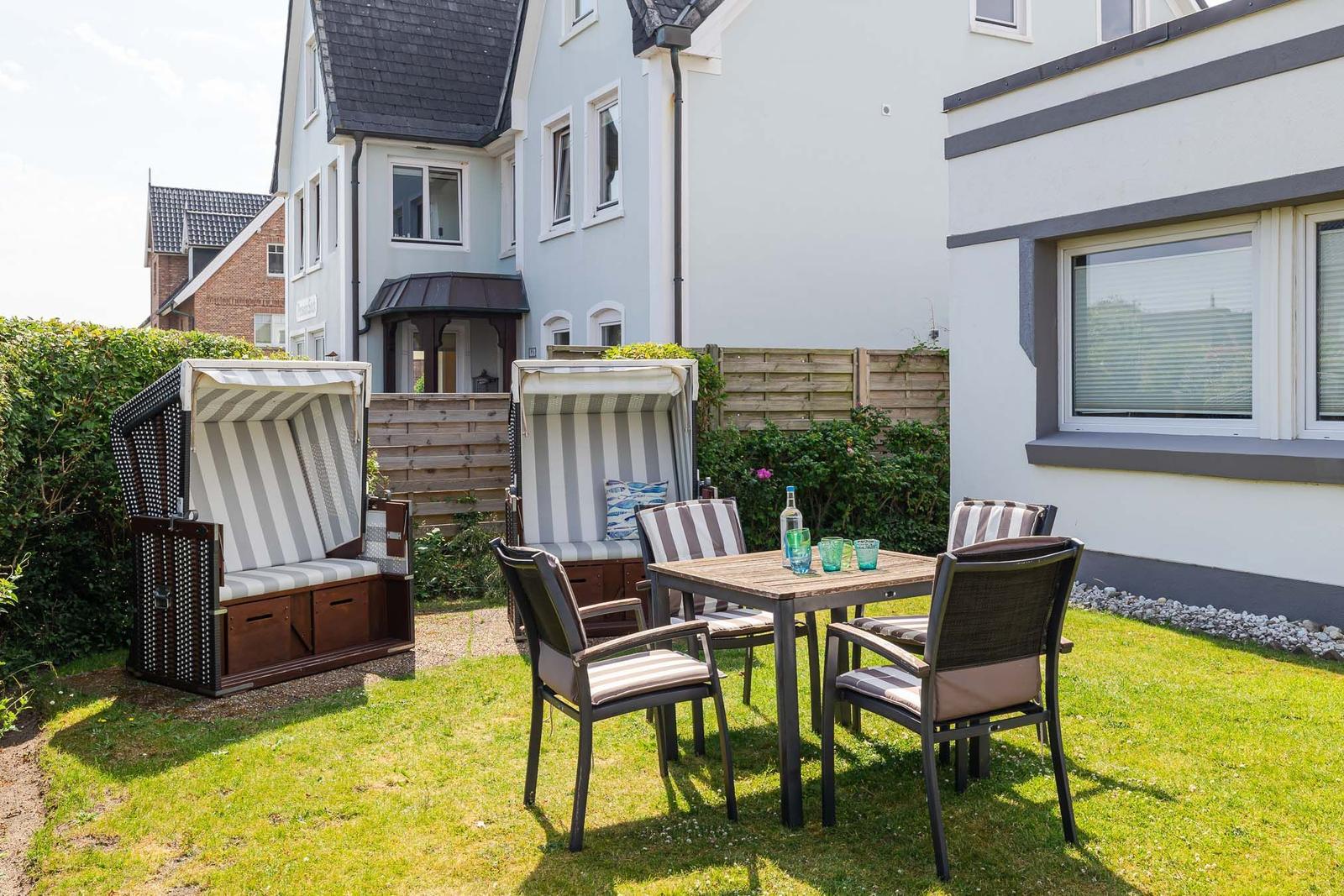 Garten mit zwei Strandkörben, Tisch und vier Stühlen auf Rasen.