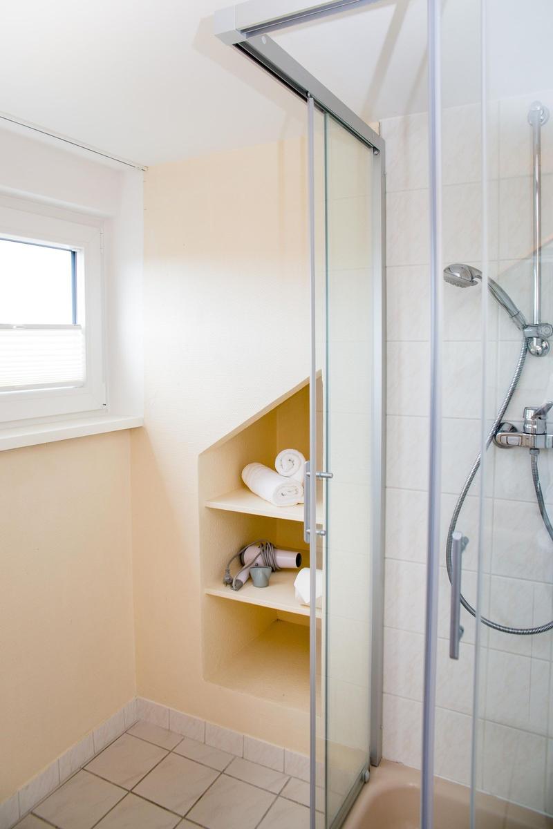 Bad mit Dusche, Fenster und eingebautem Regal mit Handtuch und Föhn.