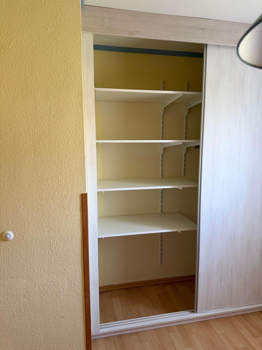 Leerer Schrank mit weißen Regalen und Schiebetüren in einem Zimmer.