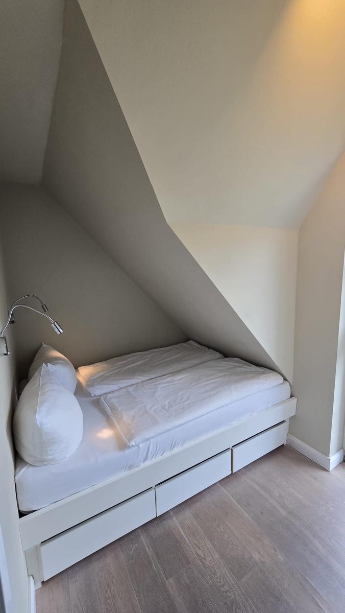 Schlafzimmer mit Dachschrägen, weißem Bett und Holzboden.