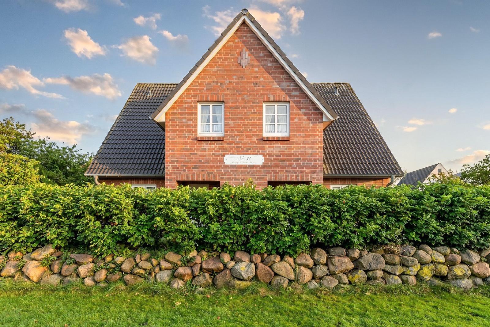 Rotes Backsteinhaus mit Dach und Hecke. Steinmauer im Vordergrund.