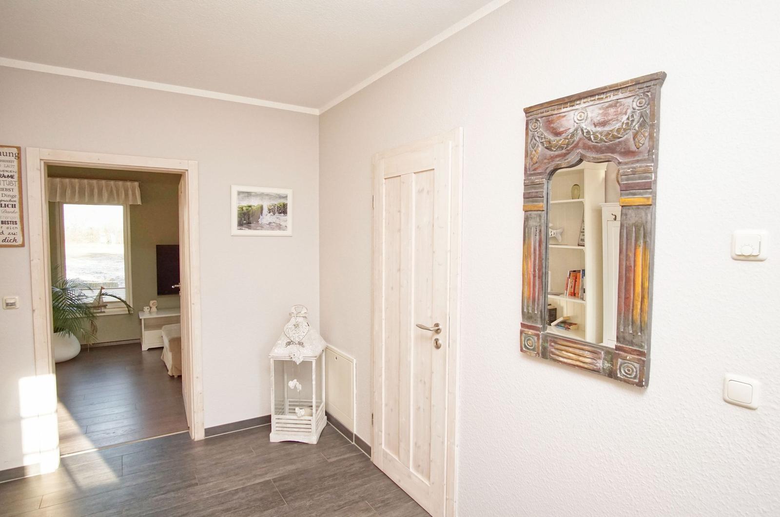 Flur mit Tür und Spiegel, Blick in Schlafzimmer mit Fenster und Pflanze.