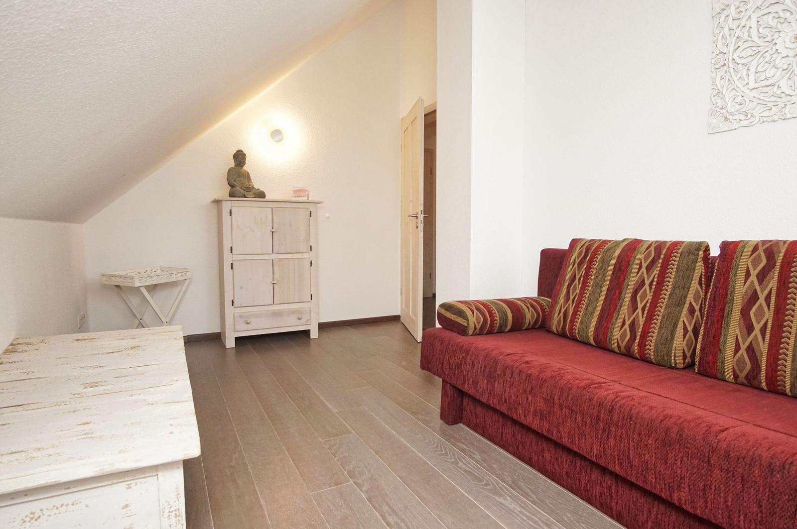 Ein Wohnzimmer mit rotem Sofa, Holzboden und weißer Schrankwand unter Dachschräge.