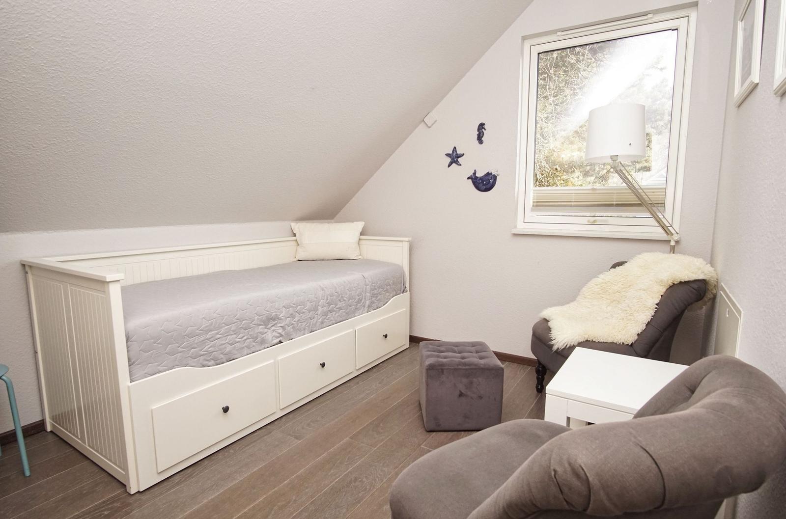 Schlafzimmer mit Bett, Sitzgelegenheit und Fenster. Wanddekoration und Holzboden.