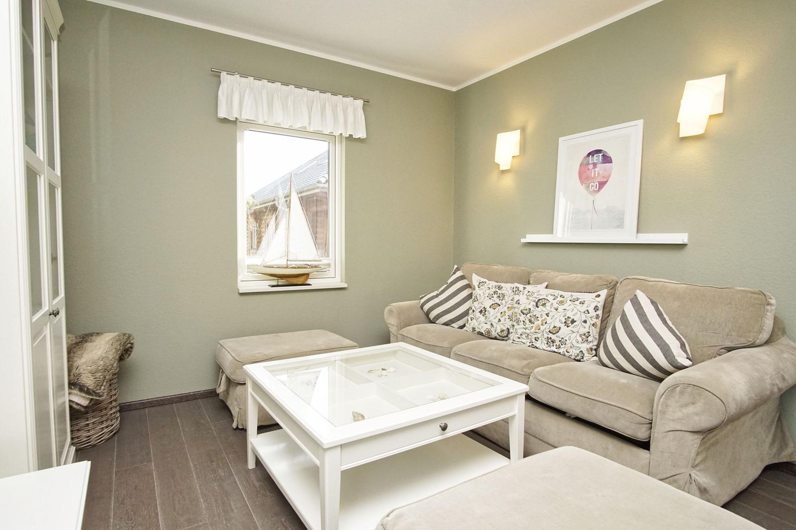 Ein Wohnzimmer mit Sofa, Tisch und Fenster. An der Wand hängt ein Bild.