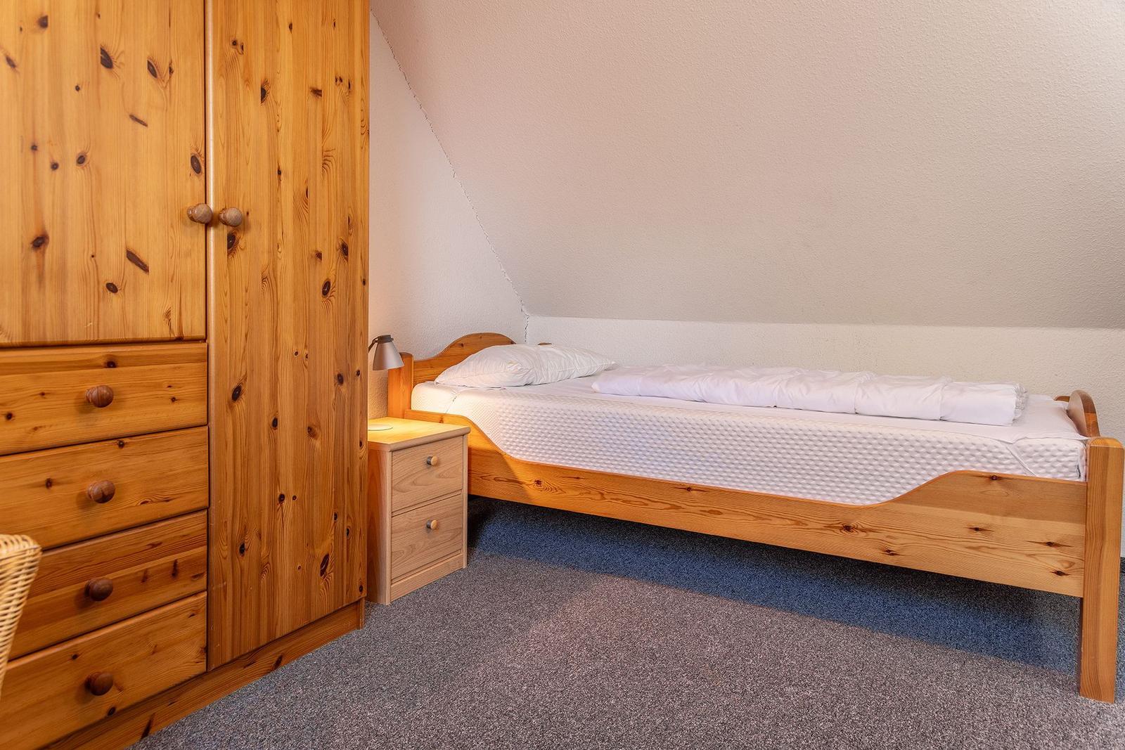 Ein Schlafzimmer mit Holzbett, Kleiderschrank und Nachttisch unter schräger Decke.