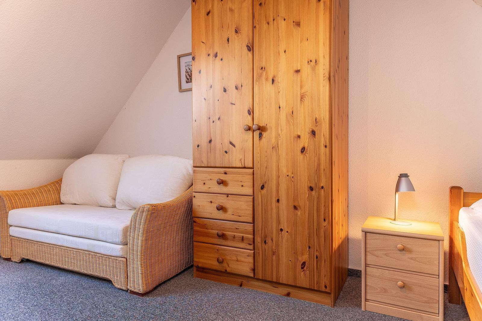 Schlafzimmer mit Holzschrank, Wicker-Sofa und Nachttisch mit Lampe.