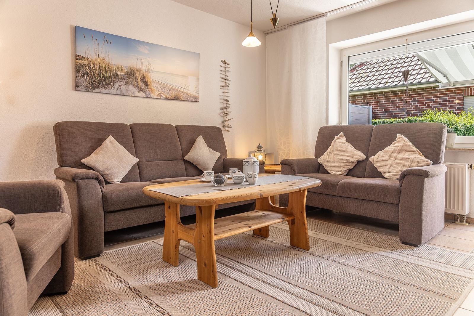 Wohnzimmer mit zwei Sofas, Holztisch und Wandbild. Fensterblick auf Garten.