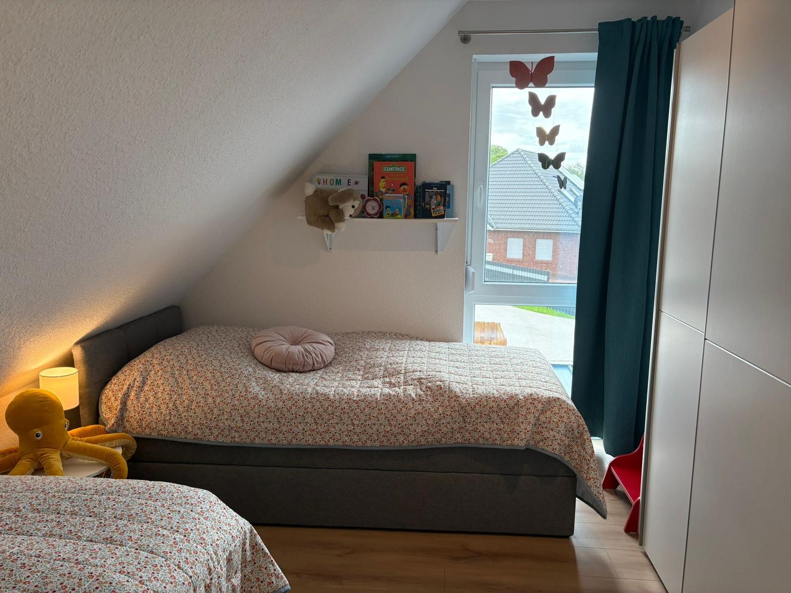 Schlafzimmer mit Dachschräge, Bett, Nachttisch und Fenster mit Blick nach draußen.