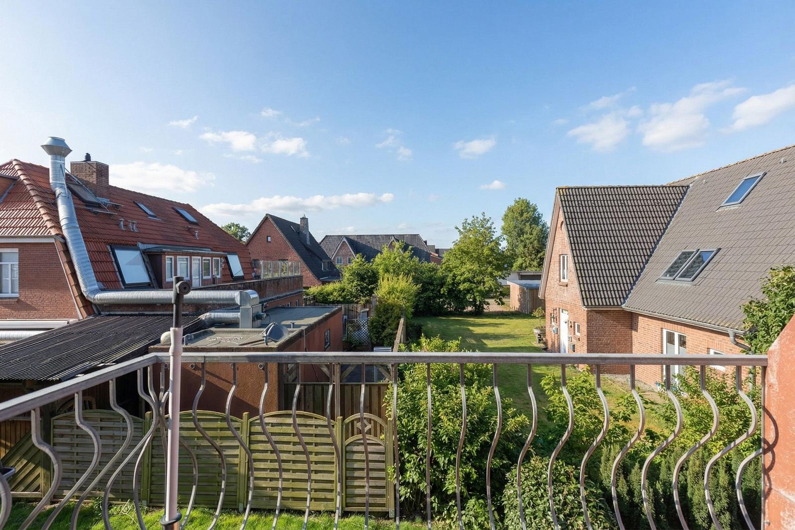 Balkon mit Blick auf Wohnhäuser und grünen Garten unter blauem Himmel.