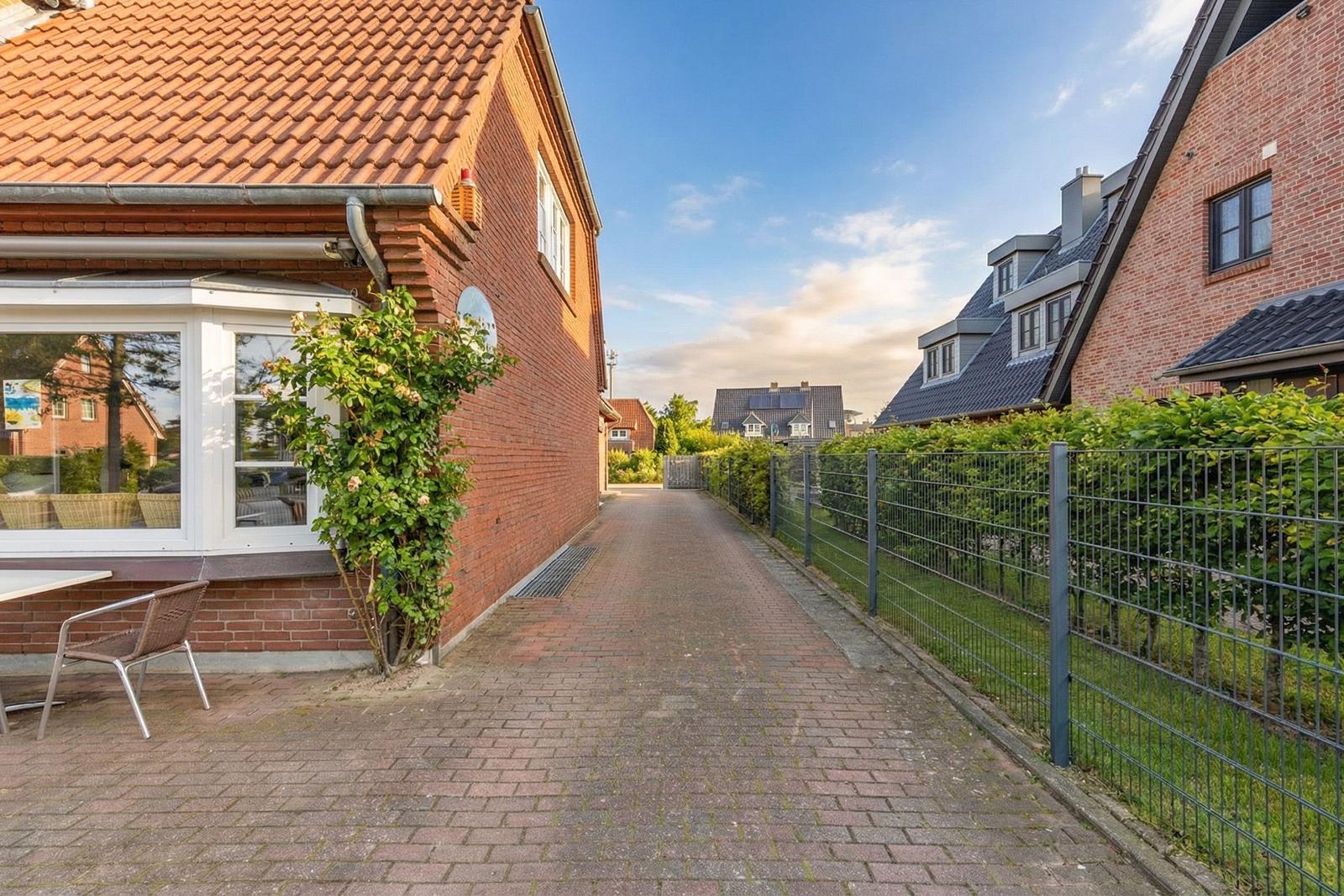 Pflasterweg zwischen zwei Häusern mit Gartenzaun und Terrasse