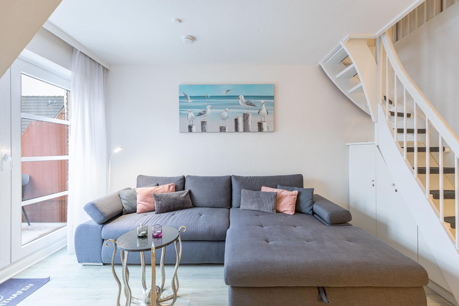 Wohnzimmer mit grauem Sofa, Bild an der Wand und Treppe zur oberen Etage.