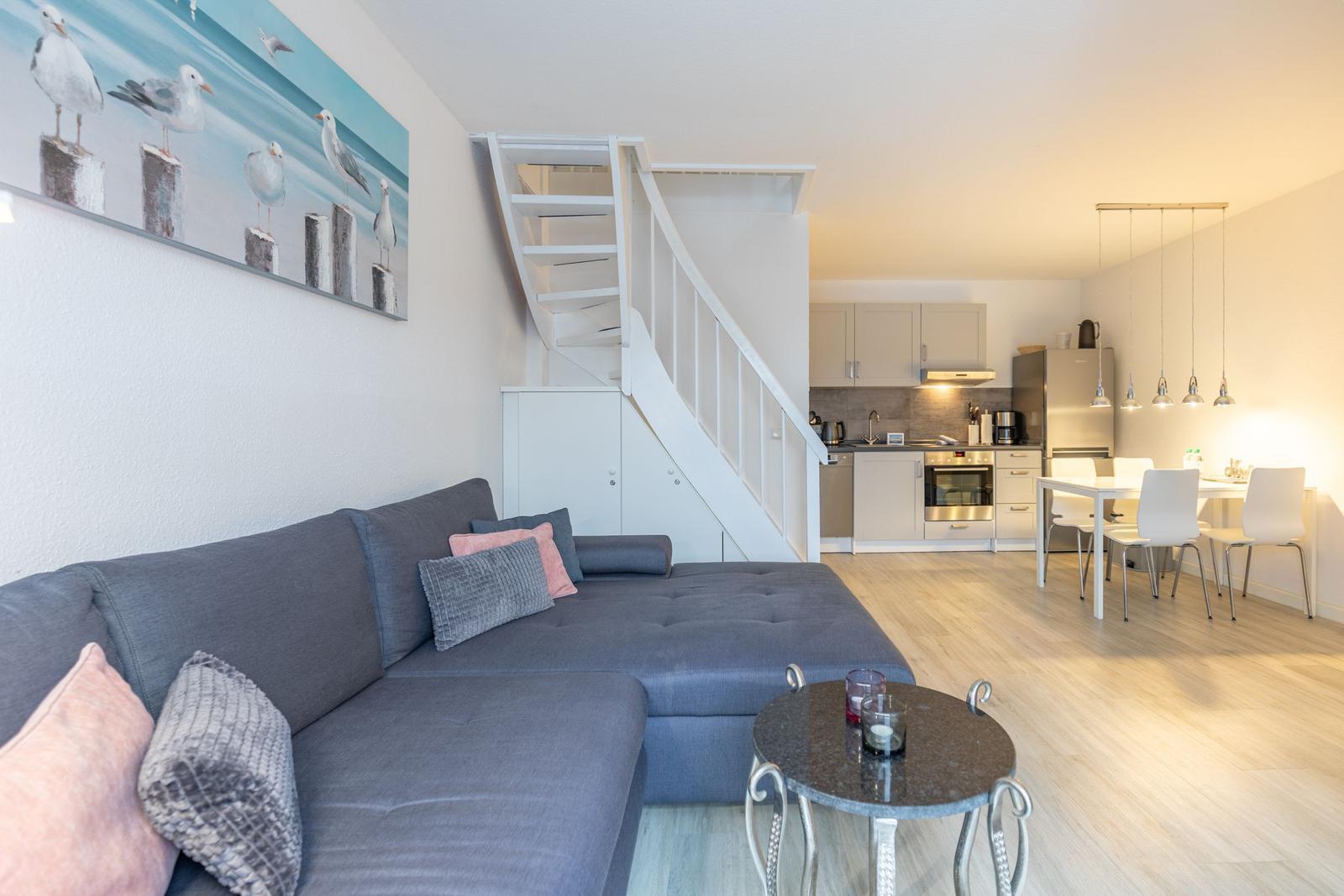 Wohnzimmer mit Sofa, Treppe und Blick in die Küche und Essbereich.