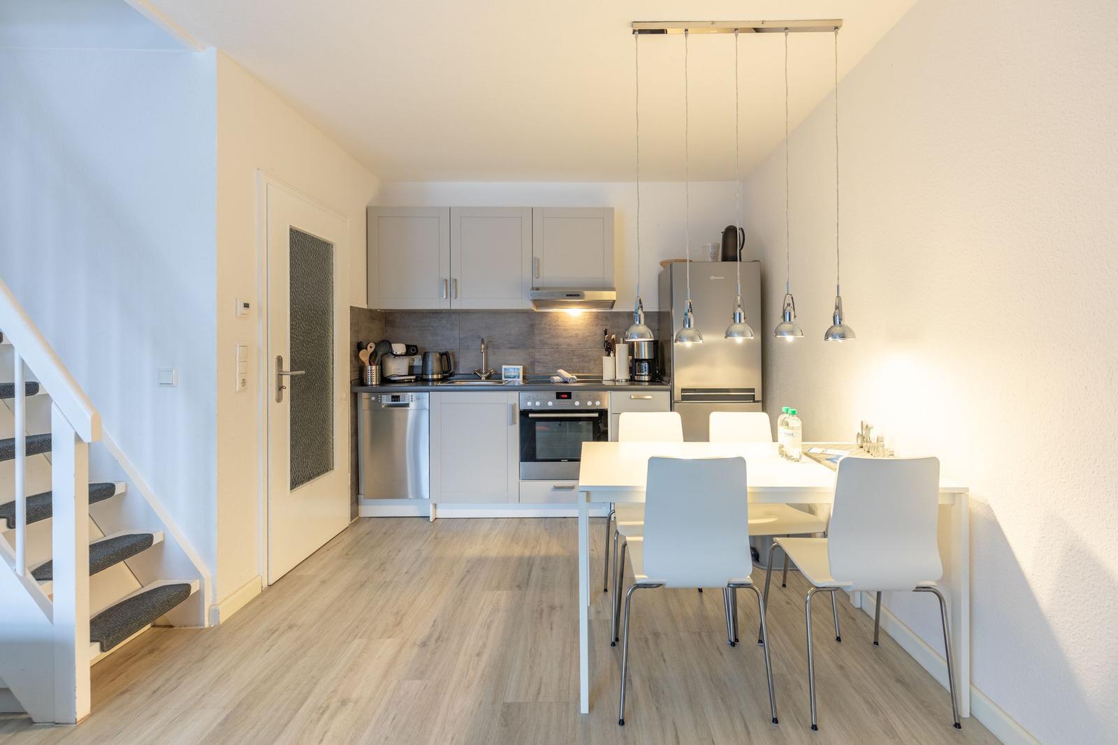 Küche mit Essbereich, weiße Stühle, hängende Lampen und Holzboden