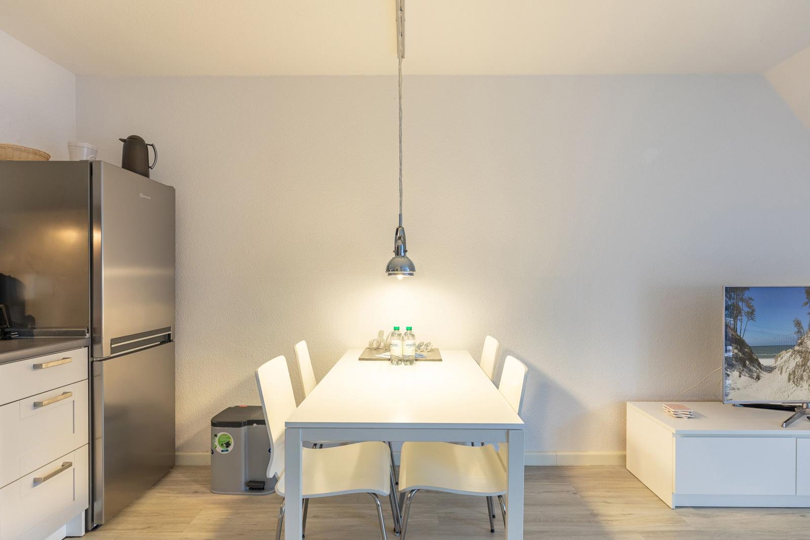 Essbereich mit Tisch, Stühlen und Küchenzeile. Fernseher auf weißem Sideboard.