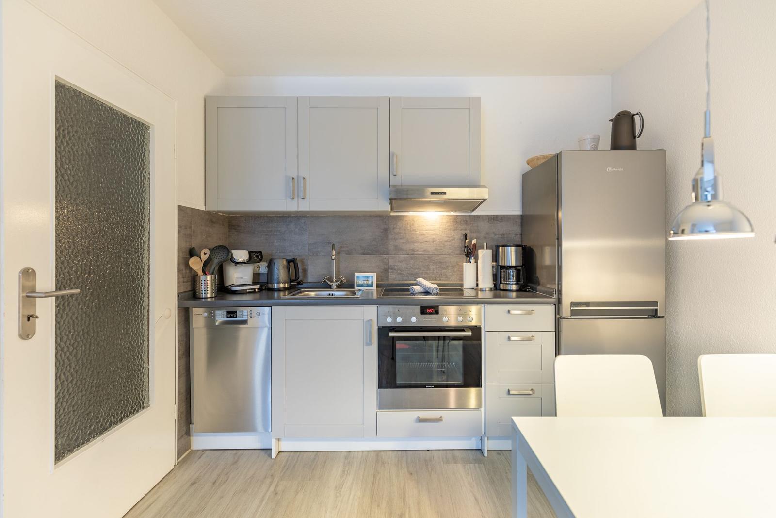 Küche mit Edelstahlgeräten, grauen Schränken und Arbeitsfläche, integriertem Herd und Kühlschrank.