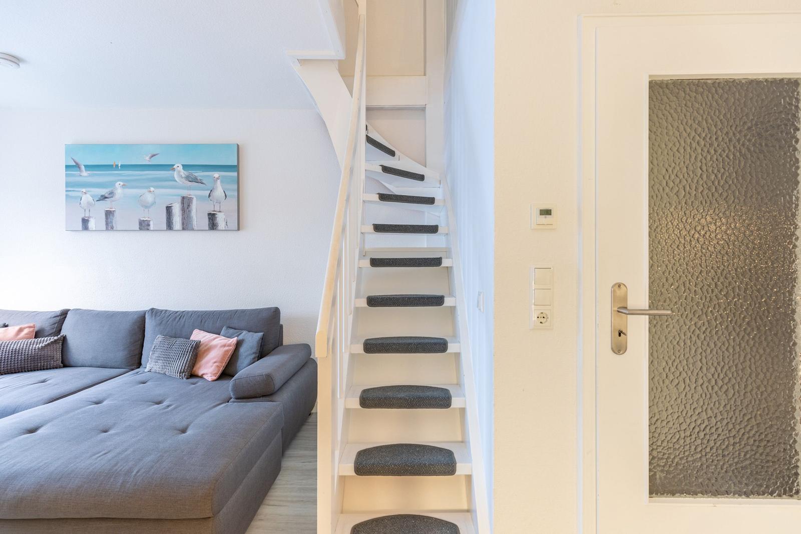 Wohnbereich mit Sofa, Treppe und Tür. Wandbild mit Möwen.