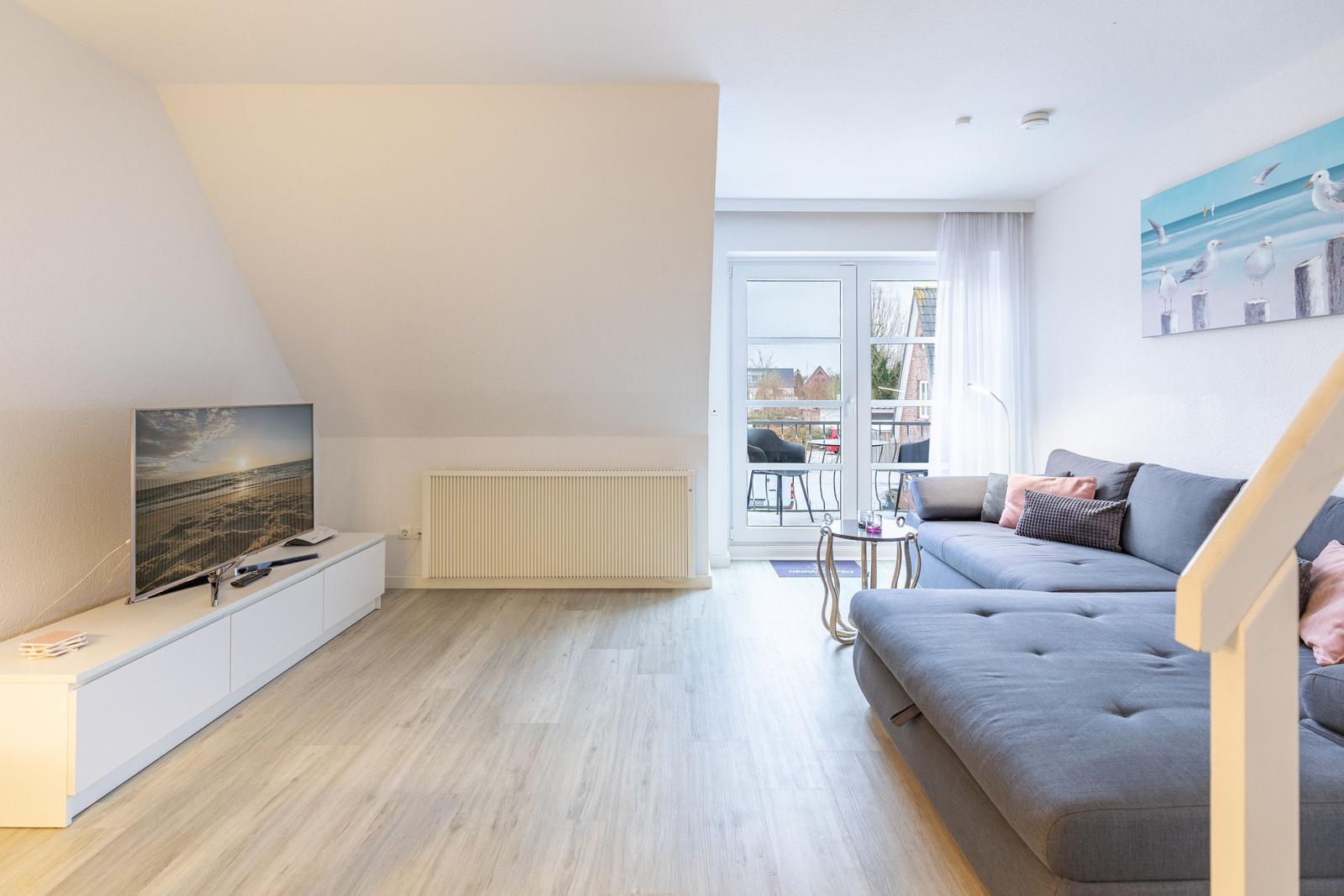 Wohnzimmer mit Sofa, Fernseher und Balkonzugang.