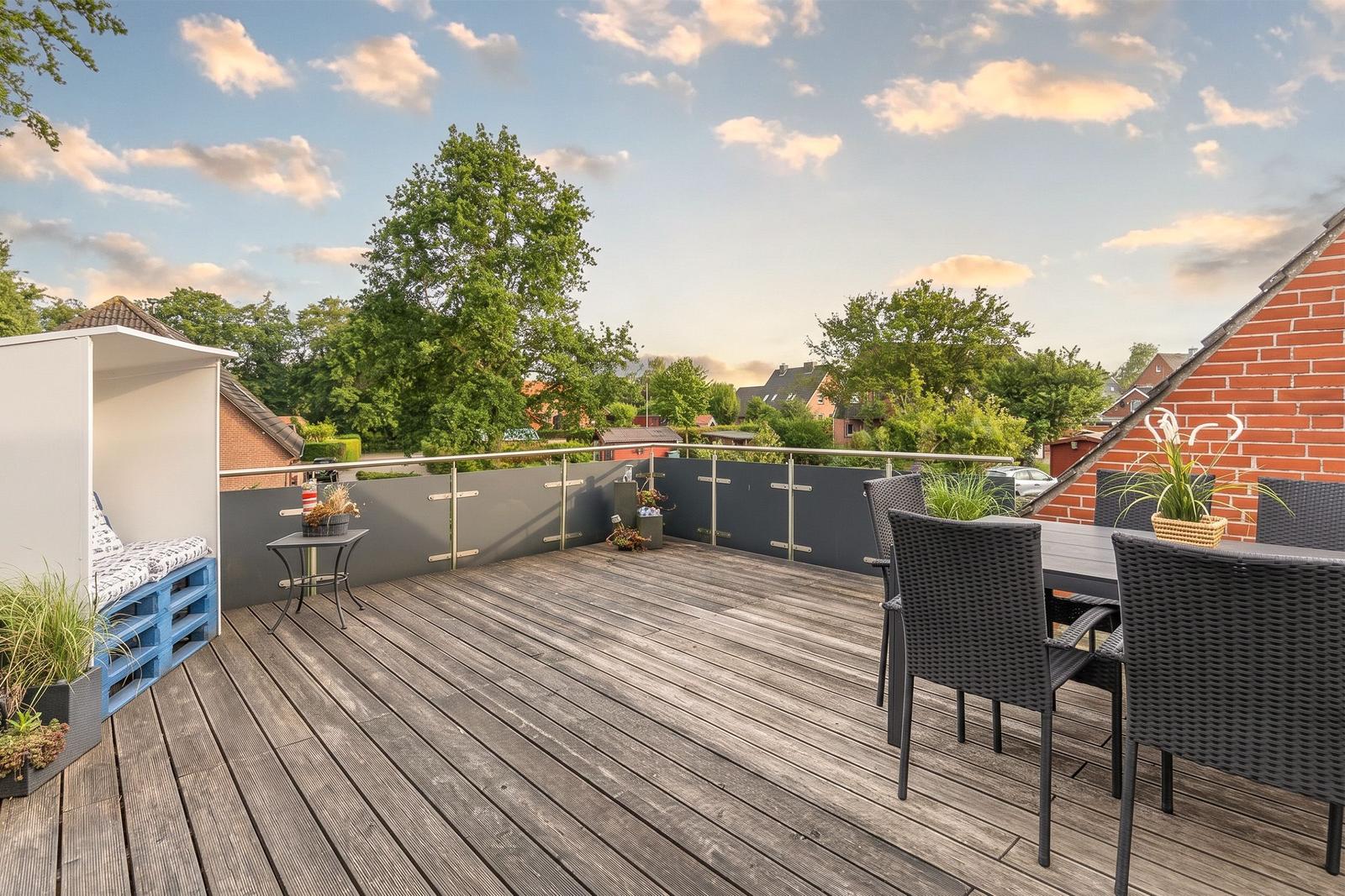Terrasse mit Sitzgelegenheit, Tisch und Stühlen. Blick auf grüne Bäume und Wohnhäuser.