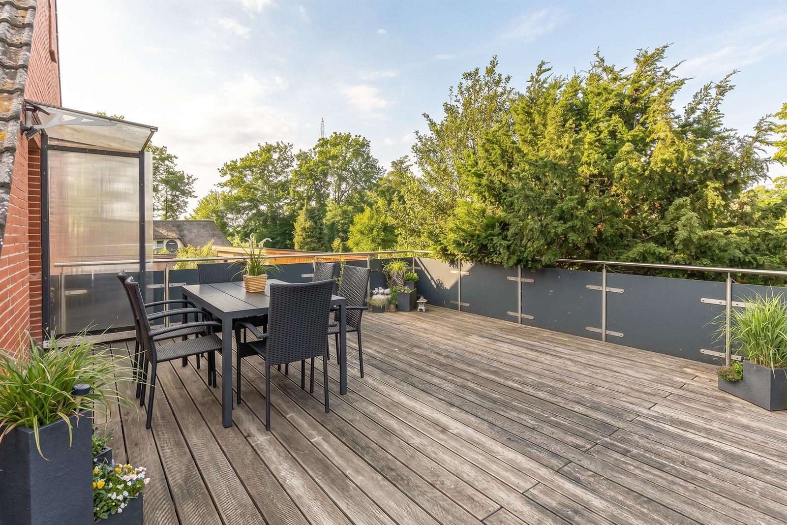 Terrasse mit Tisch und Stühlen, Pflanzen und Blick auf Bäume.