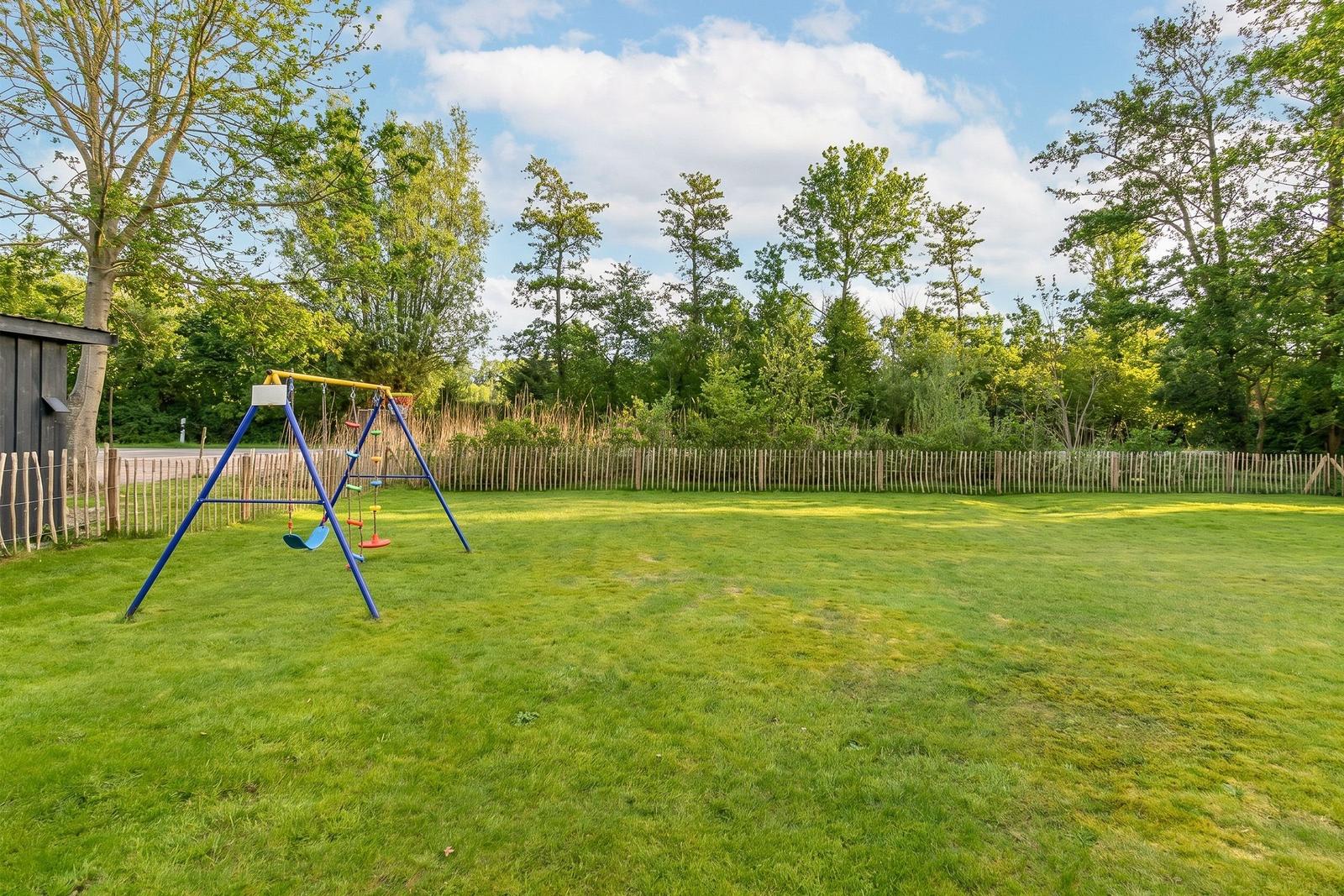 Grüner Rasen mit Kinderspielplatz und Holzzaun im Hintergrund.