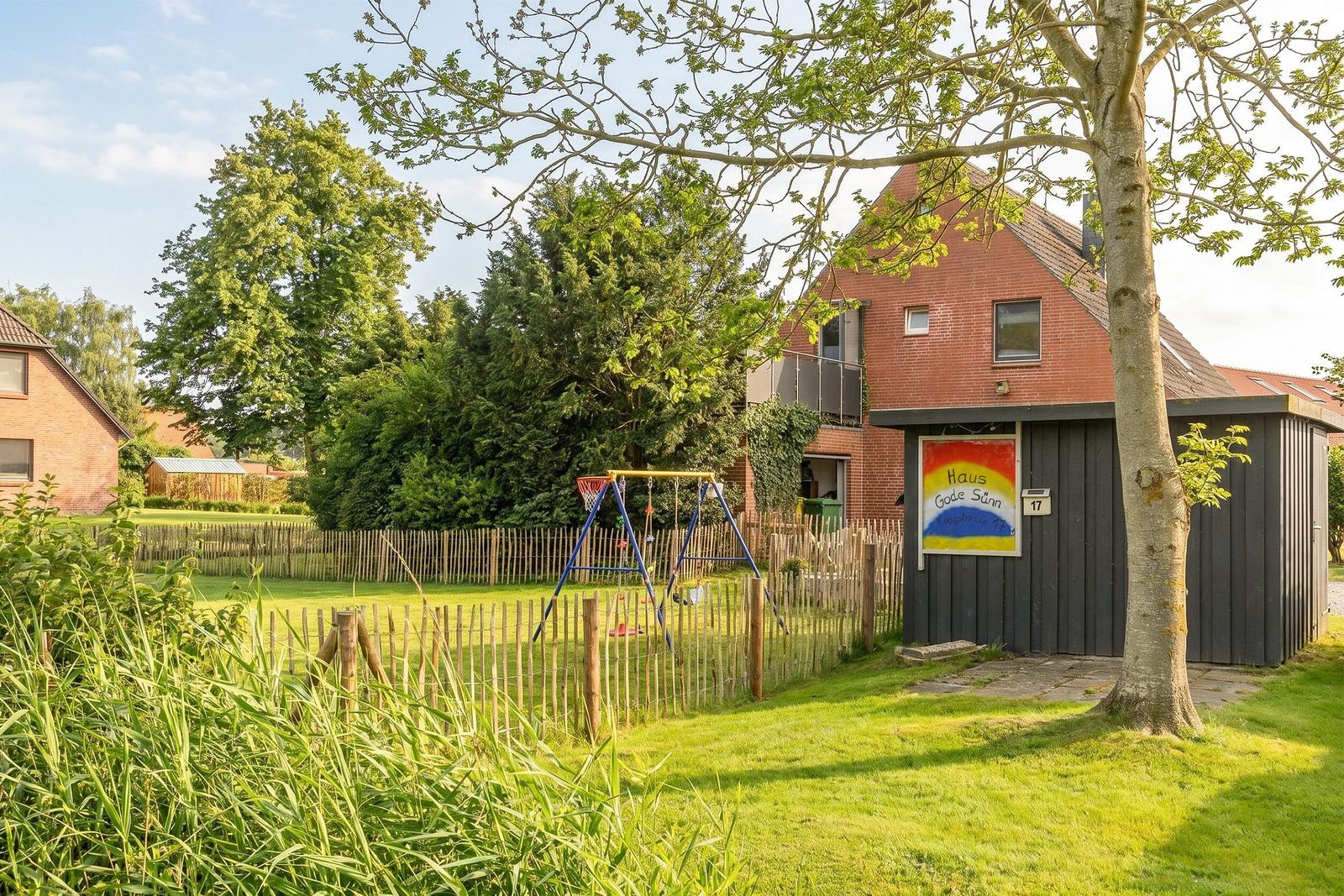 Haus mit Garten, Spielplatz und Bäumen. Eingangstür mit Schild.
