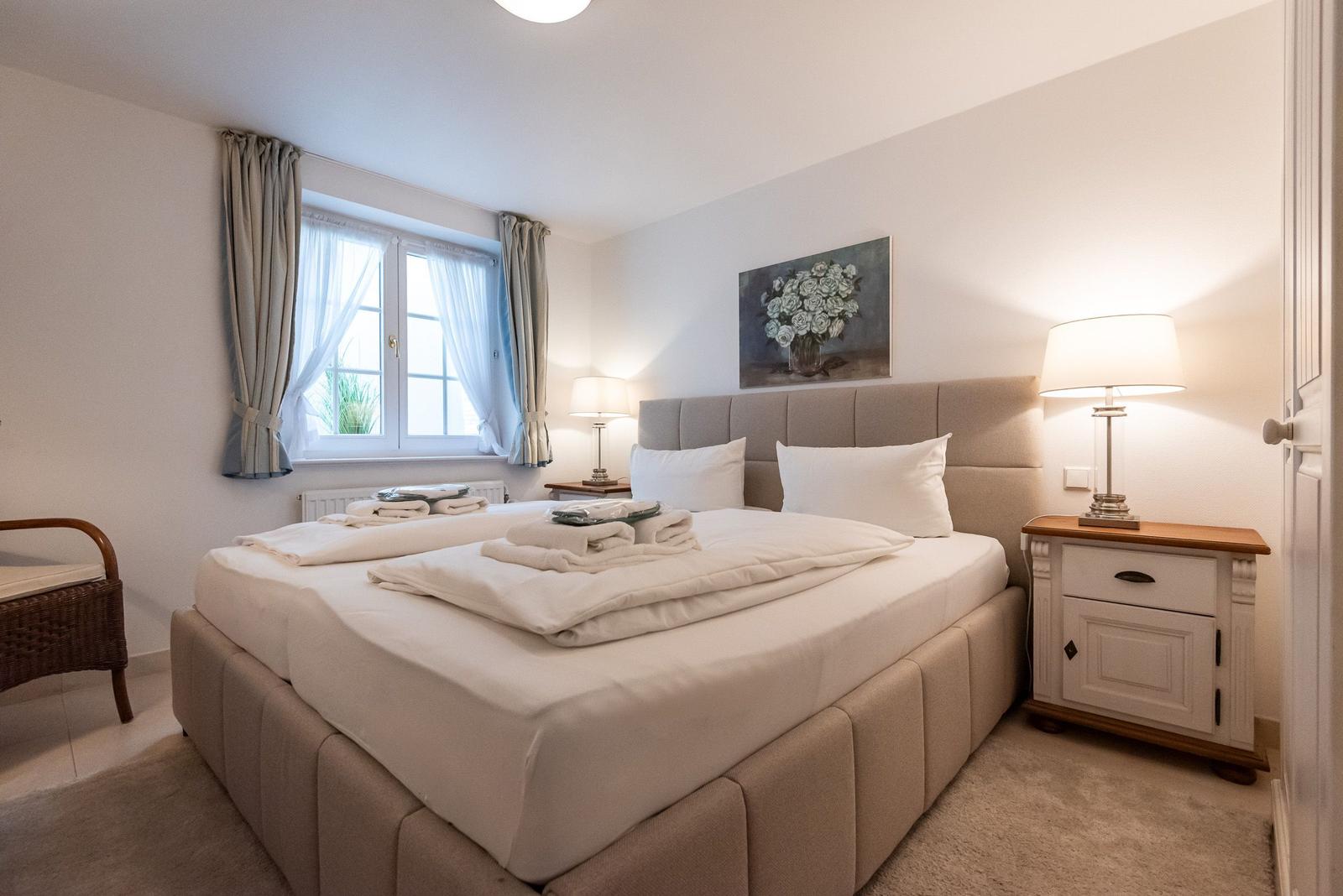 A bedroom with bed, nightstand, and window. Folded towels are on the bed.