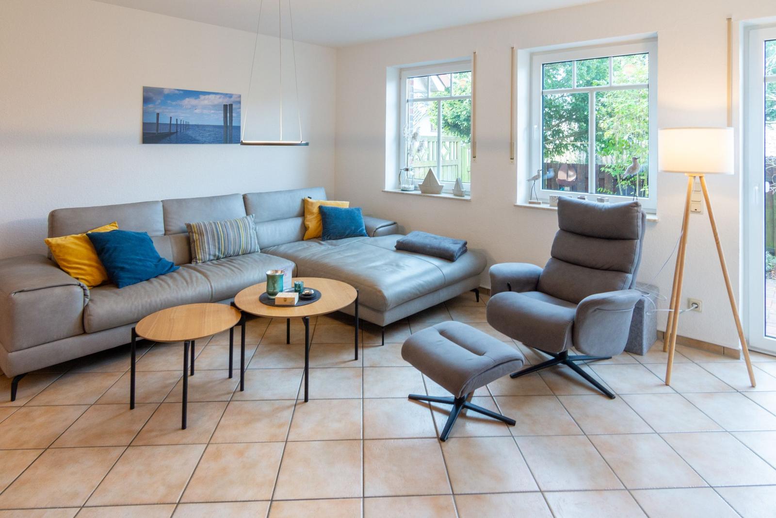 Ein Wohnzimmer mit grauem Sofa, zwei runden Tischen und einem Sessel mit Fußhocker.