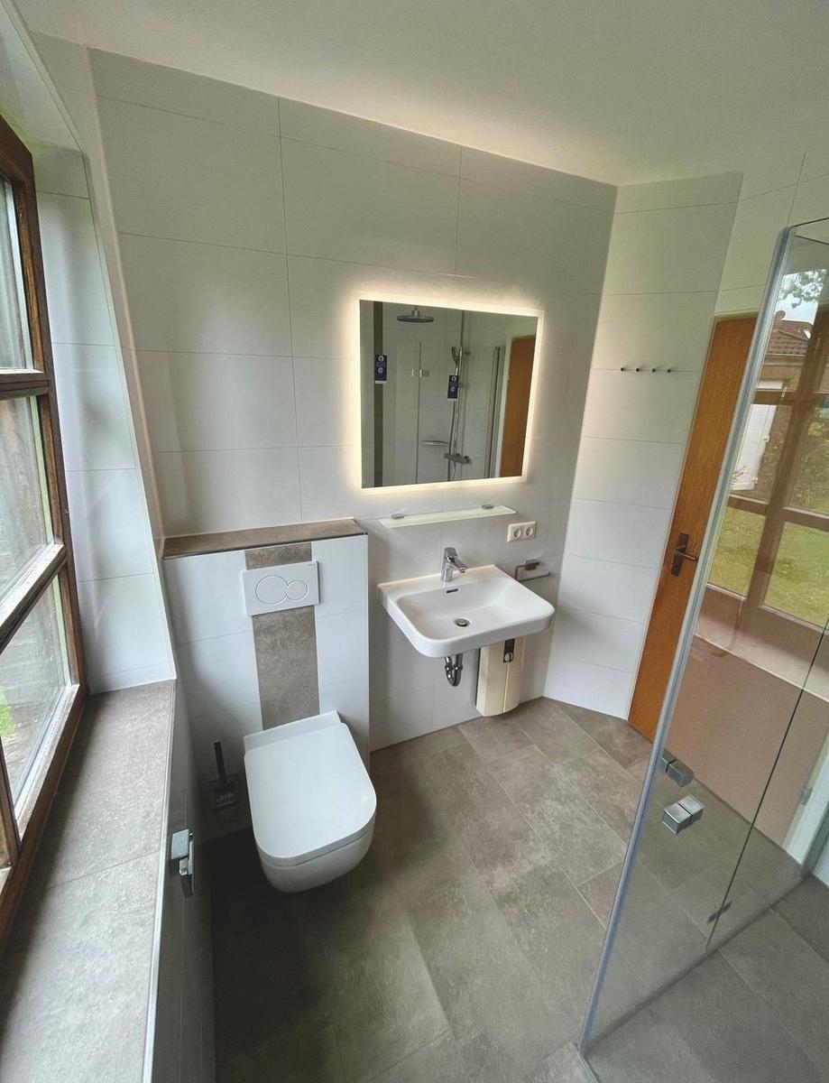 Badezimmer mit Toilette, Waschbecken und Dusche mit Glaswand.