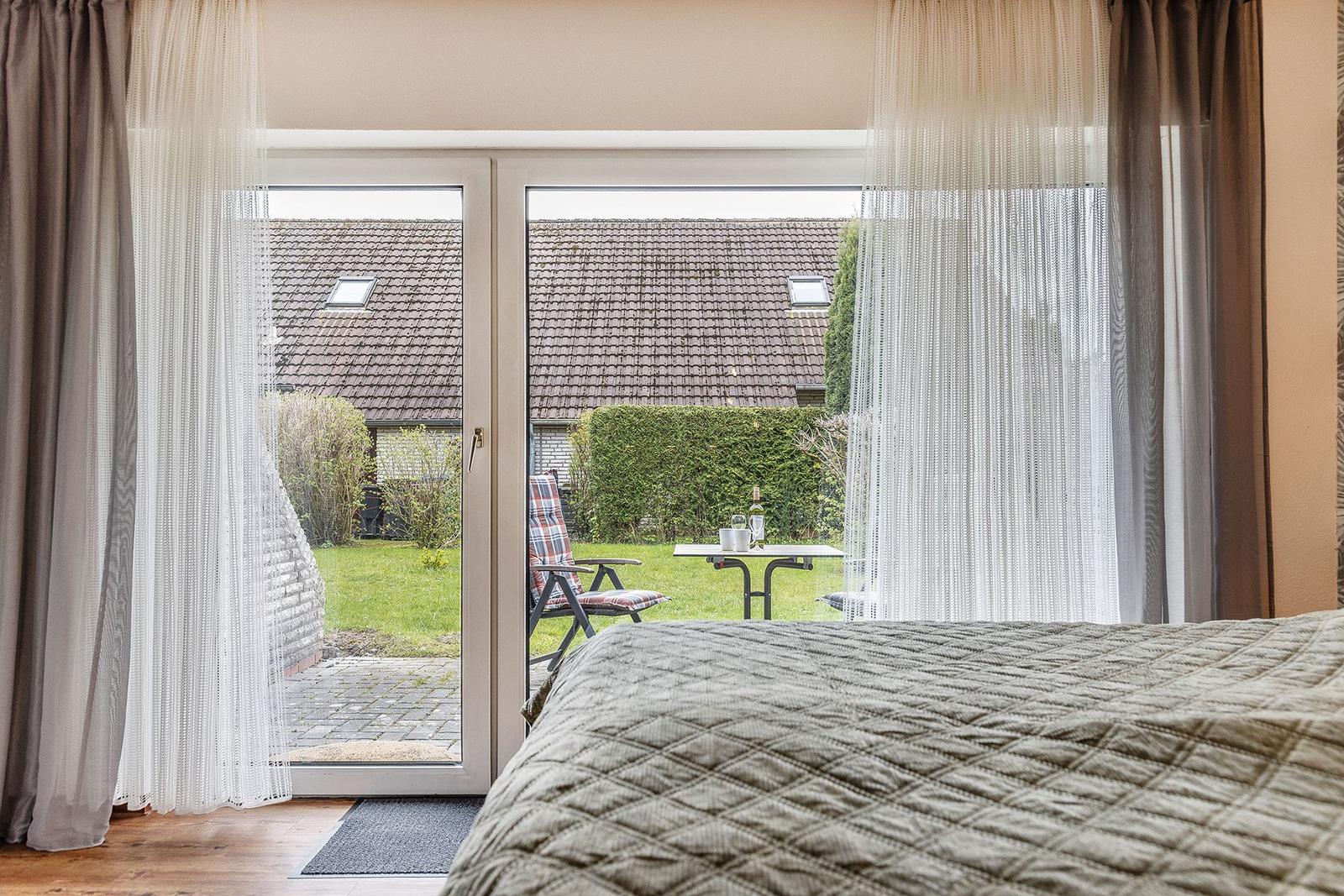Durch Glastüren führt ein Blick auf einen Garten mit Stuhl und Tisch.