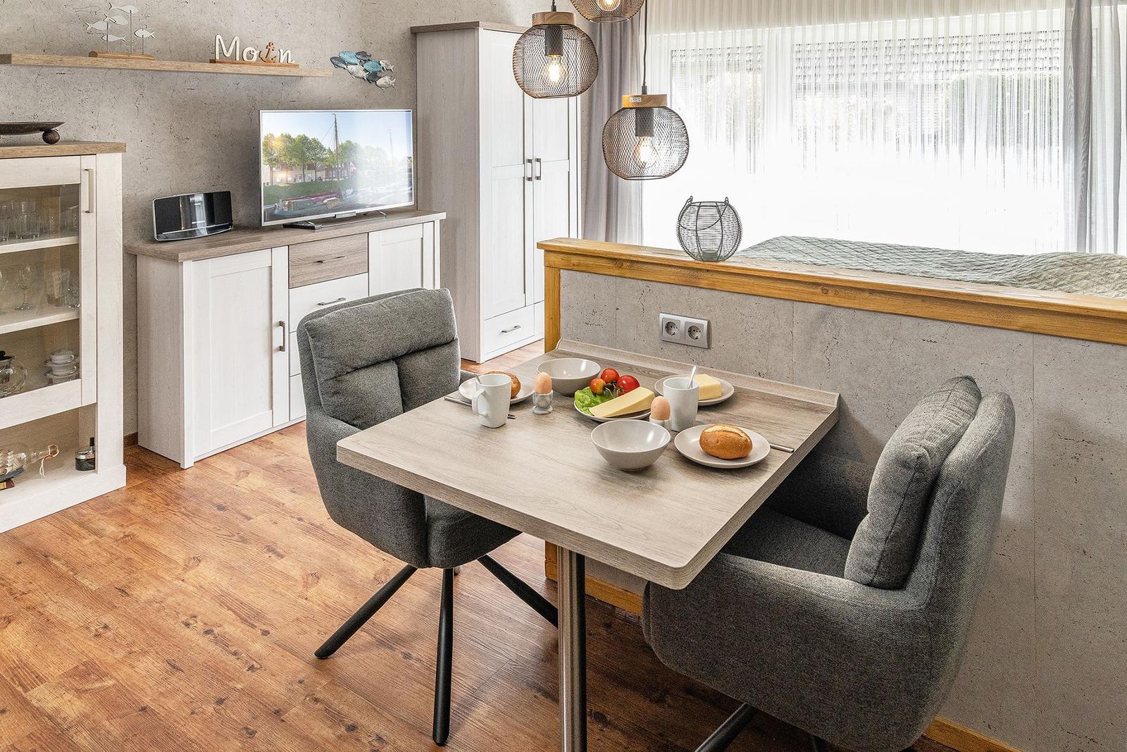 Esstisch mit zwei Stühlen, Fernseher und Fenster mit Vorhängen.