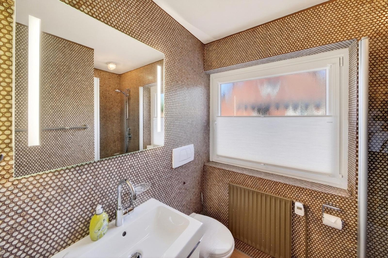 Badezimmer mit Waschbecken, Spiegel, Toilette und Fenster.