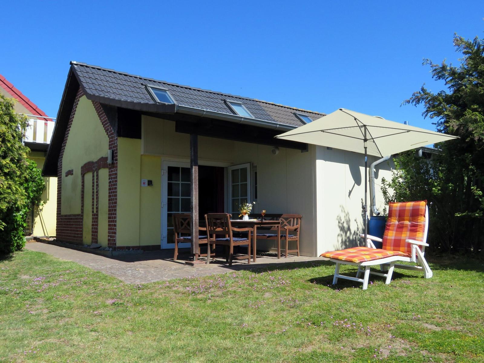 Haus mit Terrasse, Tisch, Stühlen und Liegestuhl unter Sonnenschutz.