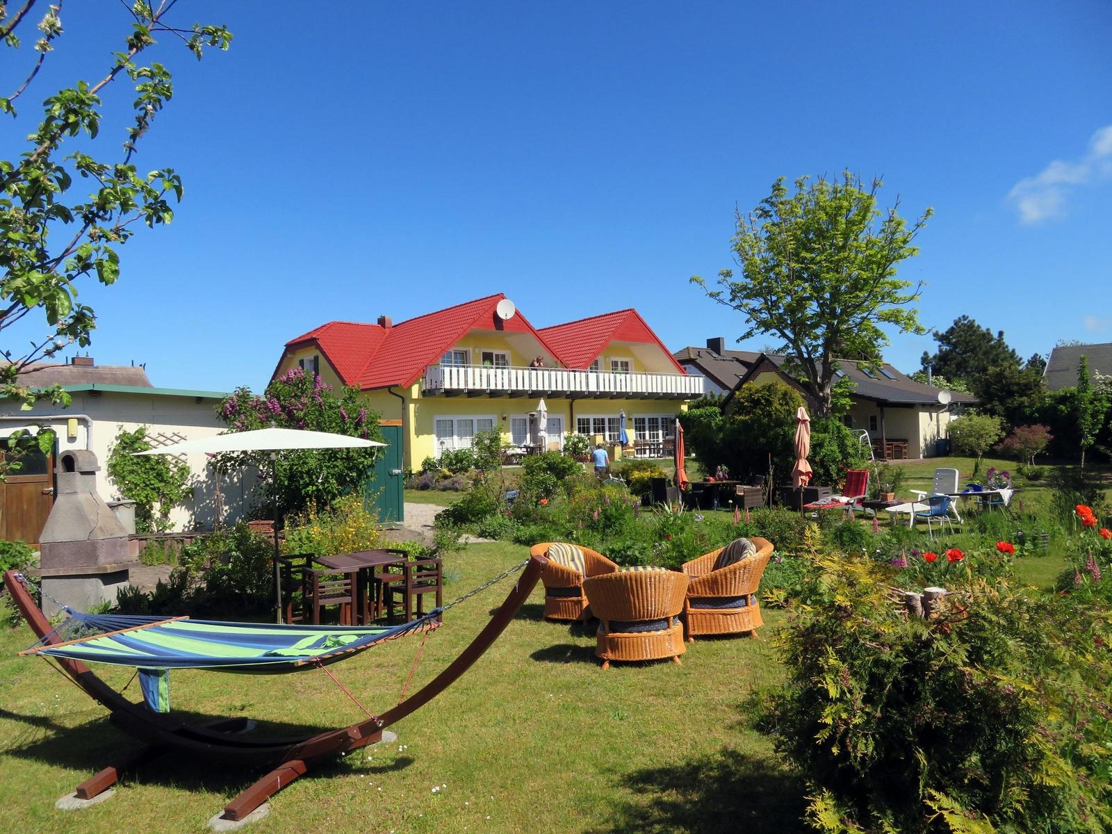Garten mit Hängematten, Gartenmöbeln und gelbem Haus mit rotem Dach.