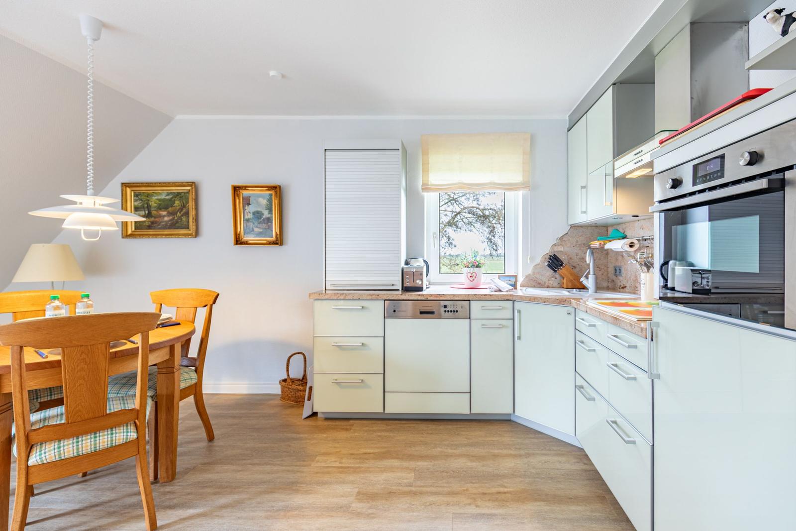 Kitchen with dining area, light cabinets, and wooden floor. Window with garden view.