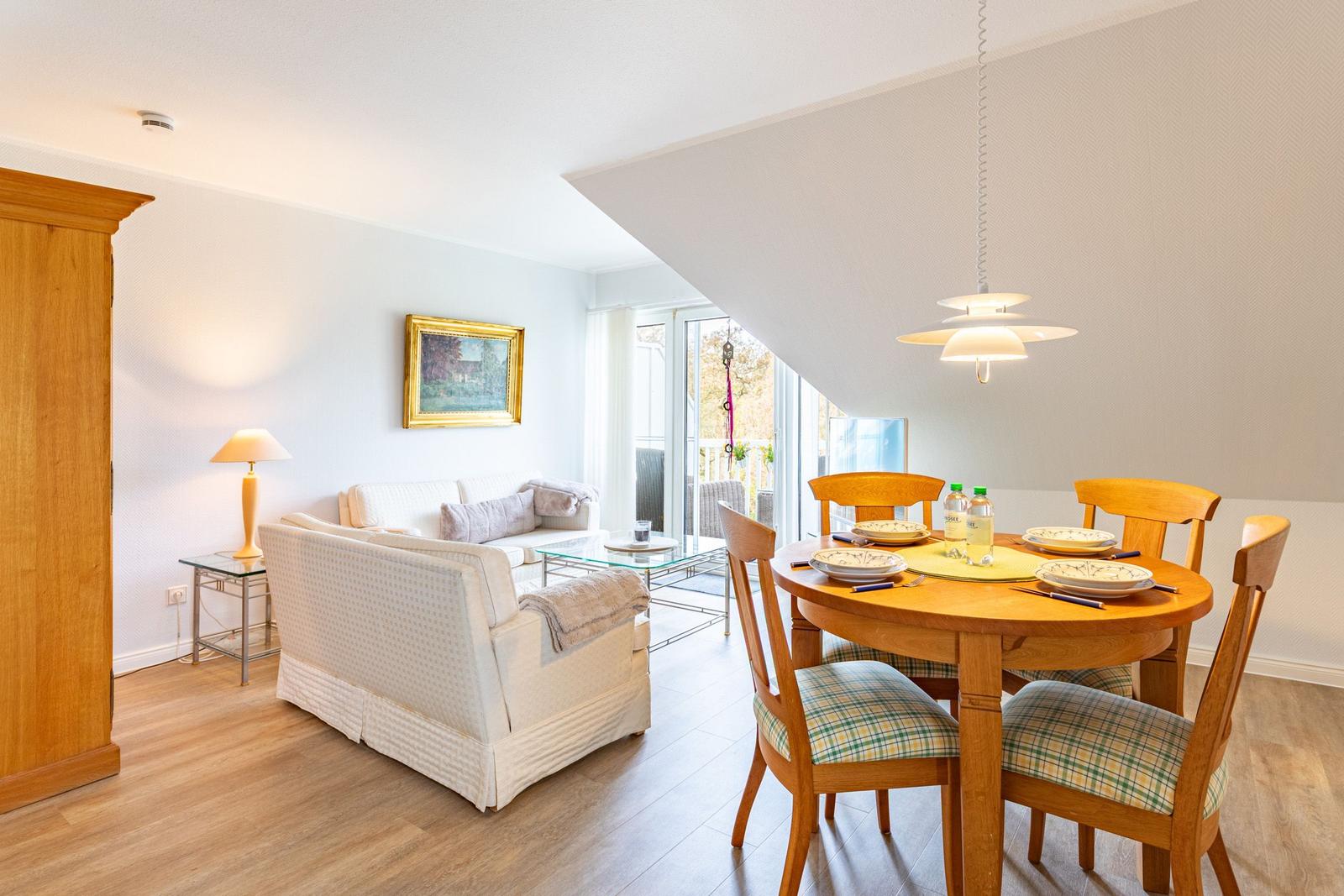 Living and dining area with wooden table, chairs, and sofa. Glass door to terrace.